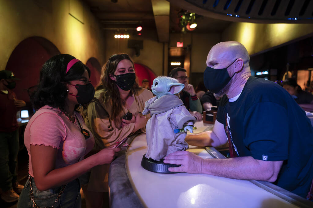 FILE - Bartender Guy Klender, right, shares a light moment with customers while celebrating Star Wars Day at Scum and Villainy Cantina, a bar located on Hollywood Blvd, in Los Angeles, Tuesday, May 4, 2021. California is bringing back a statewide indoor mask mandate. Gov. Gavin Newsom's administration announced the new mandate will start Wednesday, Dec. 15 and last until Jan. 15, 2022. The order comes as the per capita rate of new coronavirus cases in California has jumped 47% in the past two weeks. (AP Photo/Jae C. Hong, File)