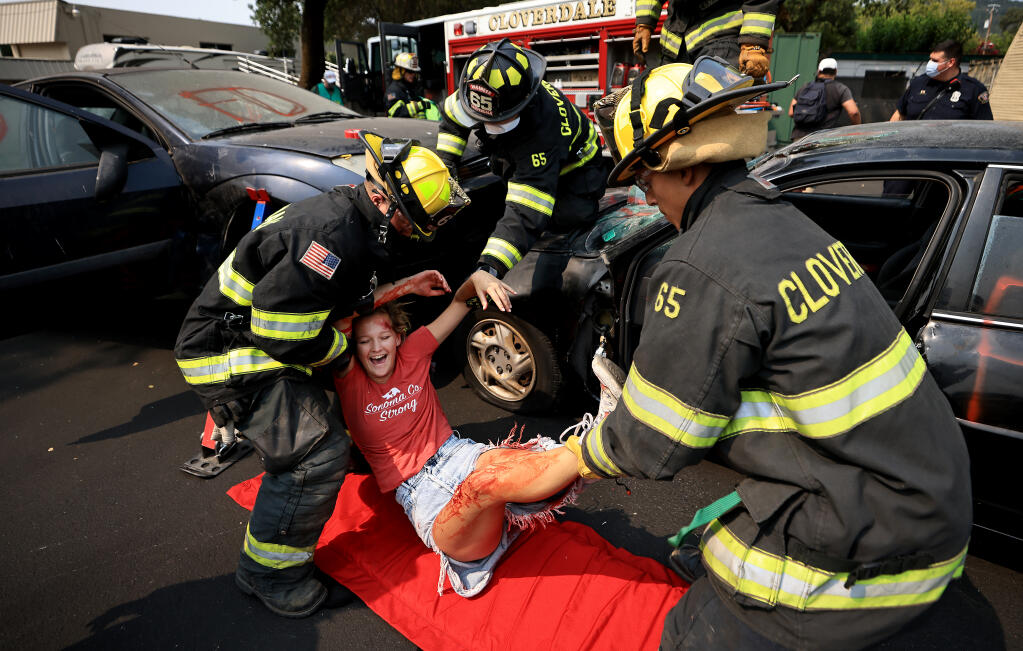 Gracie McNulty, 19, attempts to stifle a laugh as Northern Sonoma County firefighters, Colby Jenkins,  Andre Gluch and David Alvarez participate in an extrication drill during the Northern Sonoma County Fire and Earthquake Expo, Saturday, August 7, 2021 in Cloverdale.  (Kent Porter / The Press Democrat) 2021