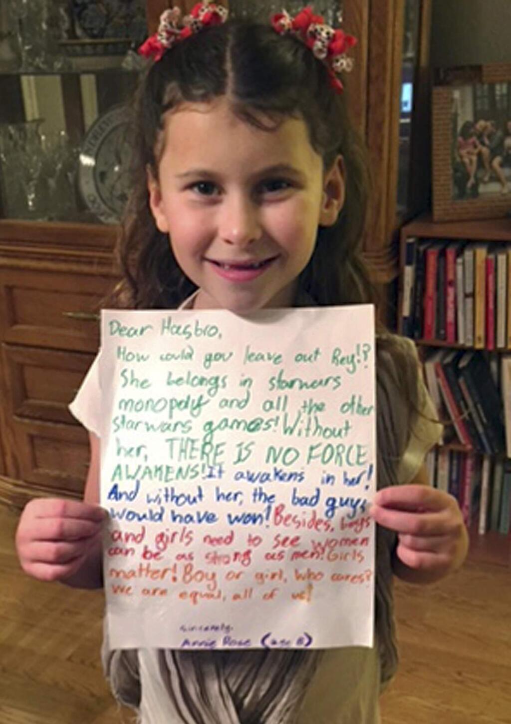 In this January 2016 photo provided by Carrie Goldman, her daughter, Annie Rose, holds a letter in Evanston, Ill., that she wrote to Hasbro asking why the female character Rey was omitted from a Monopoly set based on 'Star Wars: The Force Awakens,' when she is a main character and crucial to the story. Hasbro responded that they would add Rey to a Star Wars version of Monopoly by the end of the year. Eighteen months later, Annie Rose and others are still waiting. (Carrie Goldman via AP)