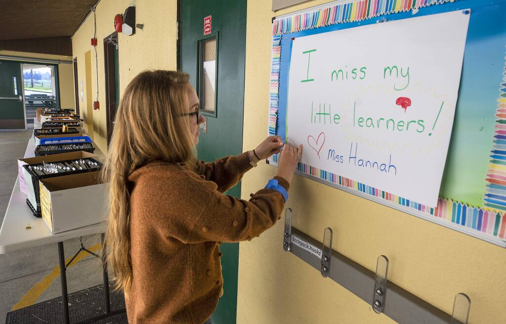 Hannah Long, a transitional kindergarten teacher at Two Rock Elementary, hangs a sign for her students to read when they pick up their homework packets at the rural west county school. (photo by John Burgess/The Press Democrat)