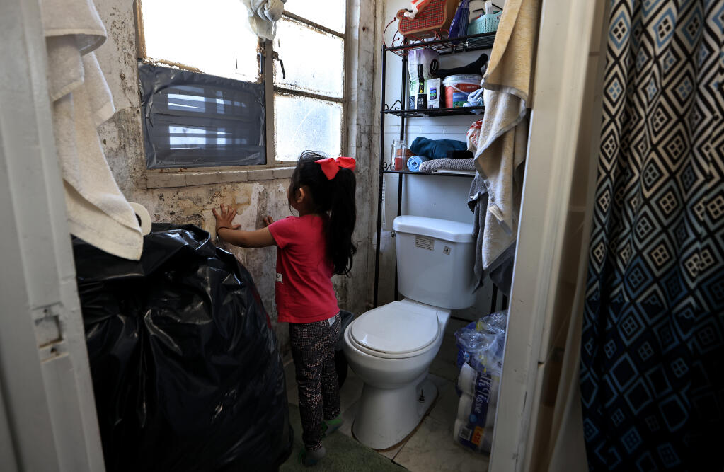 In this photo taken during the Press Democrat’s January investigation into living conditions at the former Gold Coin motel in Santa Rosa, Valentina Nunez, 4, peers out a bathroom window of the mold-covered walls (Kent Porter / The Press Democrat)