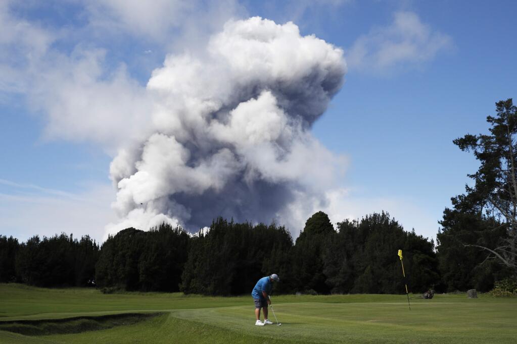 Doug Ralston plays golf in Volcano, Hawaii, as a huge ash plume rises from the summit of Kiluaea volcano Monday, May 21, 2018. Lava from Hawaii's Kilauea volcano is pouring into the sea and setting off a chemical reaction that creates giant clouds of acid and fine glass. (AP Photo/Jae C. Hong)