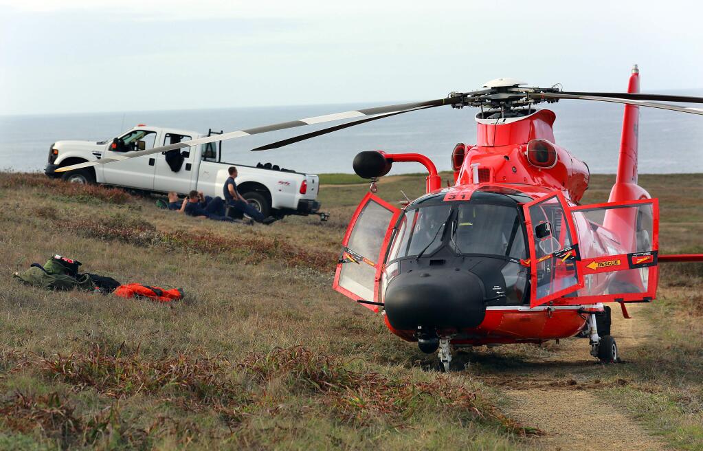 A crew from the San Francisco Coast Guard station keeps watch over a rescue helicopter stuck and unable to launch from where it landed on Monday night during a rescue of a 4 year-old boy who fell from the cliffs on Bodega Head. (JOHN BURGESS/ PD)