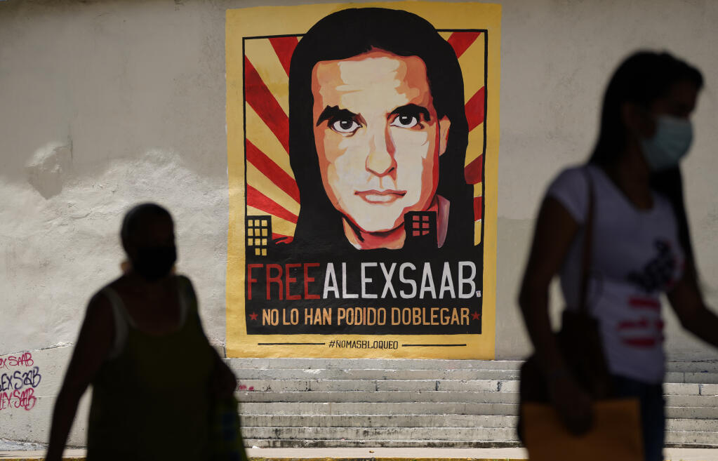 FILE - In this Thursday, Sept 9, 2021, file photo, pedestrians walk near a poster asking for the freedom of Colombian businessman and Venezuelan special envoy Alex Saab, in Caracas, Venezuela. Saab, a top fugitive close to Venezuela's socialist government has been put on a plane to the U.S. to face money laundering charges, a senior U.S. official confirmed Saturday, Oct. 16, 2021. (AP Photo/Ariana Cubillos, File)