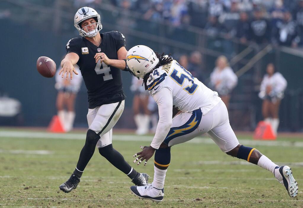 Oakland Raiders quarterback Derek Carr dumps off a pass under pressure by San Diego Chargers defensive end Melvin Ingram, during their game in Oakland on Sunday, November 11, 2018. The Chargers defeated the Raiders 20-6.(Christopher Chung/ The Press Democrat)