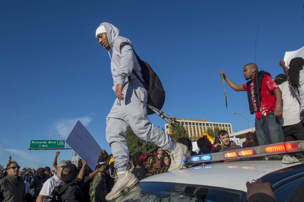 A protester walks across the top of a police car as hundreds of protesters demonstrating against the fatal police shooting of Stephon Clark shut down Interstate 5 in both directions in downtown Sacramento, Calif., Thursday, March 22, 2018. Protesters decrying this week's fatal shooting of the unarmed black man marched from Sacramento City Hall and onto the nearby freeway Thursday, disrupting rush hour traffic and holding signs with messages like 'Sac PD: Stop killing us!' (Renee C. Byer/The Sacramento Bee via AP)