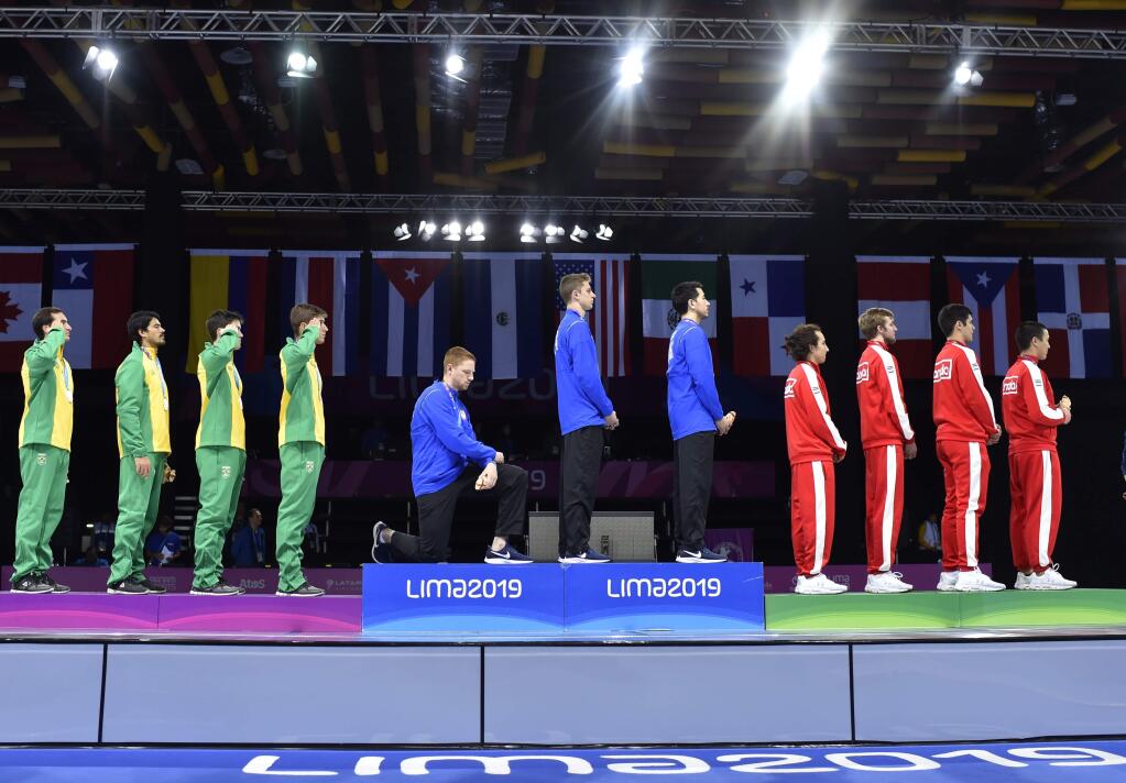 In this Friday, Aug. 9, 2019 photo, released by Lima 2019 News Services, Race Imboden of the United States takes a knee, as teammates Mick Itkin and Gerek Meinhardt stand on the podium after winning the gold medal in team's foil, at the Pan American Games in Lima, Peru. 'Racism, gun control, mistreatment of immigrants, and a president who spreads hate are at the top of a long list' of America's problems, Imboden said in a tweet sent after his medals ceremony. 'I chose to sacrifice my moment today at the top of the podium to call attention to issues that I believe need to be addressed. (Jose Sotomayor/Lima 2019 News Services via AP)