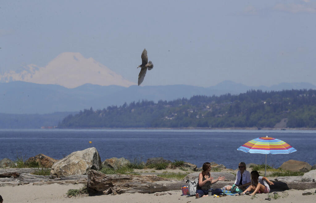 People sit outside as Mount Baker rises in the distance, in Edmonds, Wash., Saturday, May 13, 2023. (Greg Gilbert/The Seattle Times via AP)