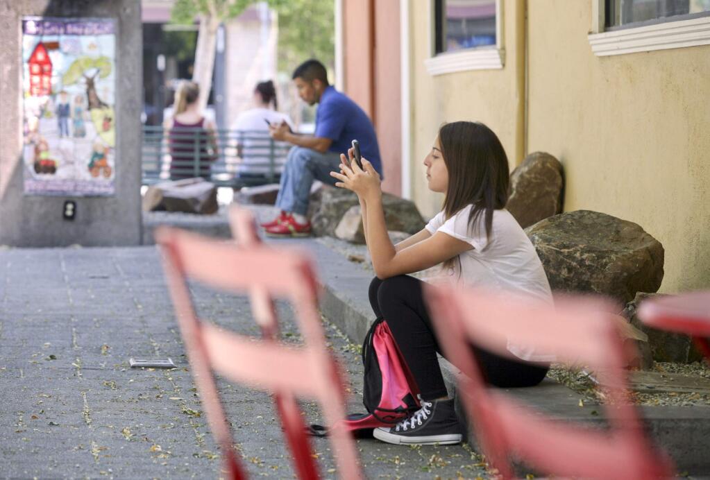Jasmine Serrano, 13 of Petaluma, has to sit on a curb as Luis Ruiz of Petaluma sits on a rock near where benches were previously located at Putnam Plaza in Petaluma on Tuesday, August 18, 2015. (SCOTT MANCHESTER/ARGUS-COURIER STAFF)