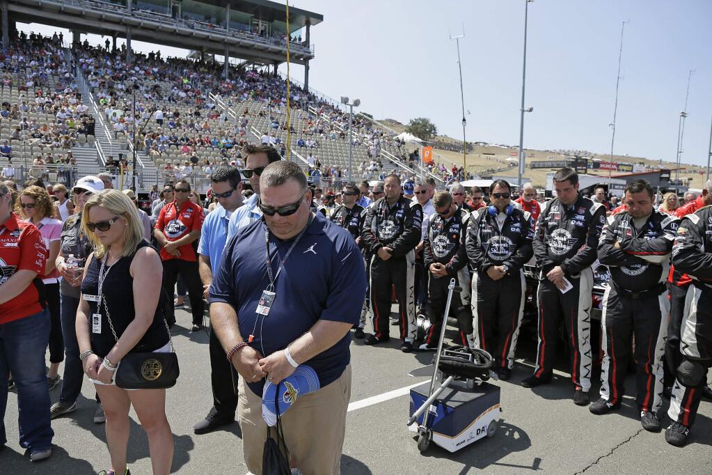 Spectators and the pit crew of Graham Rahal, at right, stand during a moment of silence for Justin Wilson before the IndyCar Grand Prix of Sonoma auto race Sunday, Aug. 30, 2015, in Sonoma, Calif. Wilson, of England, died Aug. 24 from injuries sustained at Pocono Raceway. (AP Photo/Eric Risberg)