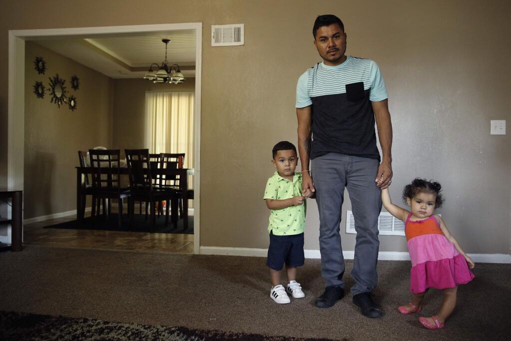 In this photo taken Tuesday, Aug. 28, 2018, Louis Alberto Enamorado Gomez stands with his daughter, Jeydi, 1, and son, Justin, 3, at their home in Grandview, Mo. Living in the U.S. since 2005, Gomez is fighting a deportation order stemming from a 2012 DUI charge because he fears what his removal would mean for his seven children, all U.S. citizens for whom he is the sole provider. (AP Photo/Charlie Riedel)