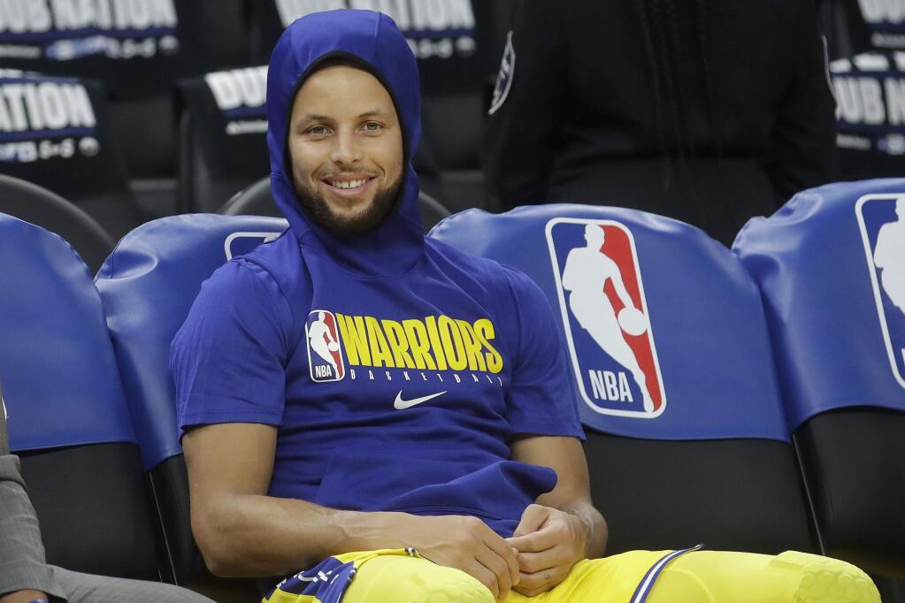 In this Thursday, Feb. 27, 2020 file photo, Golden State Warriors guard Stephen Curry smiles on the bench as players warm up before a game between the Warriors and the Los Angeles Lakers in San Francisco. Curry had hoped to play for the Warriors on Sunday, March 1 at home against the Washington Wizards, but he won't return quite yet from a broken left hand. The two-time NBA MVP has been sidelined the past four months. (AP Photo/Jeff Chiu, File)