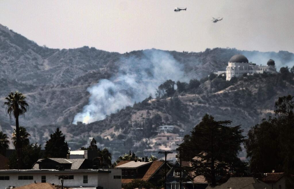 Water dropping helicopters fly over the Griffith Observatory in Los Angeles as a wildfire burns along the hillsides sending up huge plumes of smoke visible throughout the city Tuesday, July 10, 2018. Los Angeles Fire Department officials say the fire damaged some cars parked in area but nobody was hurt. (AP Photo/Richard Vogel)
