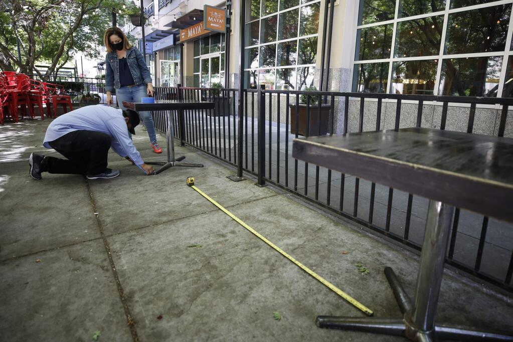 Francisco Medina, kneeling and Damaris Martinez, standing, measure the distance between tables of the outdoor dining space for social distancing at Tequila Museo Mayahuel restaurant in Sacramento, Calif., Wednesday May 20, 2020. Sacramento is expecting to receive state approval for customers to dine in this week. (AP Photo/Rich Pedroncelli)