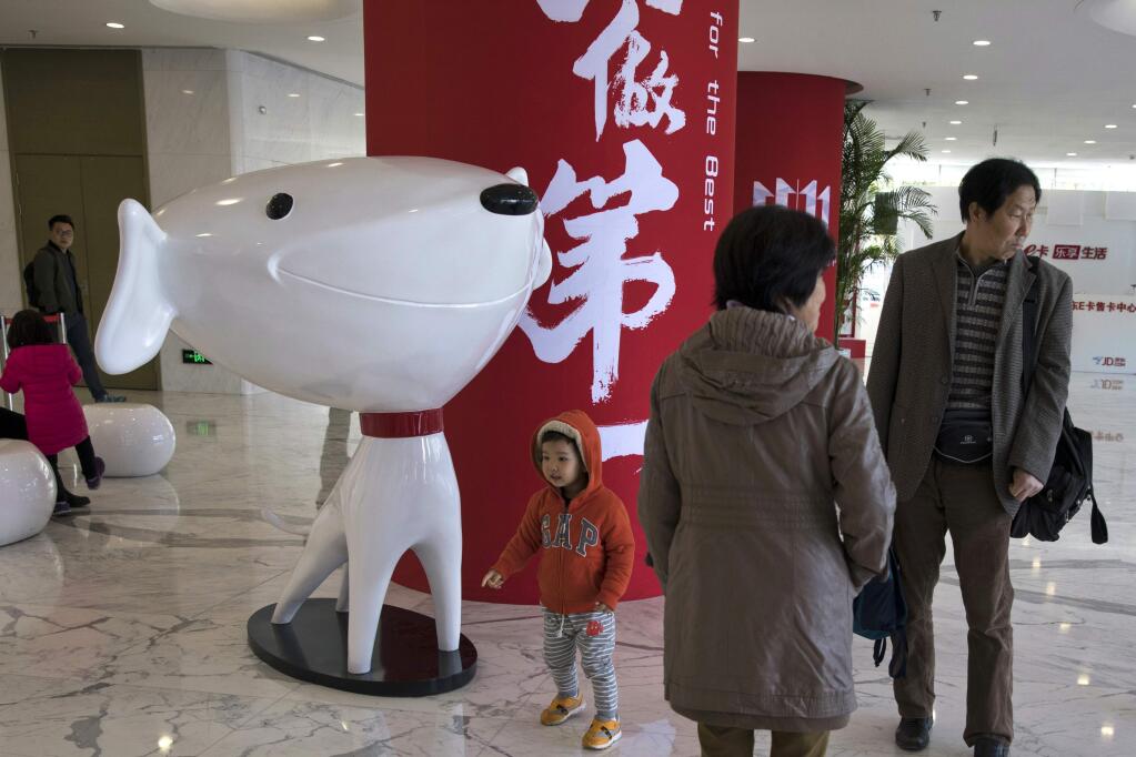In this Nov. 11, 2017, photo, a child stands near the mascot for Chinese e-commerce giant JD.com and the words for 'Be Number One' at the headquarters in Beijing, China. Google says Monday, June 18, 2018, it will invest $550 million in Alibaba's main rival JD.com as the U.S. tech giant seeks to expand in fast-growing Asian e-commerce markets. (AP Photo/Ng Han Guan)