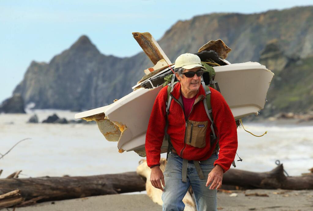 Sonoma Coast Surfriders Richard James, of Inverness carries pieces of a wrecked fiberglass boat from the North Jenner Beach at the mouth of the Russian River on Tuesday, January 17, 2017. (John Burgess/The Press Democrat)