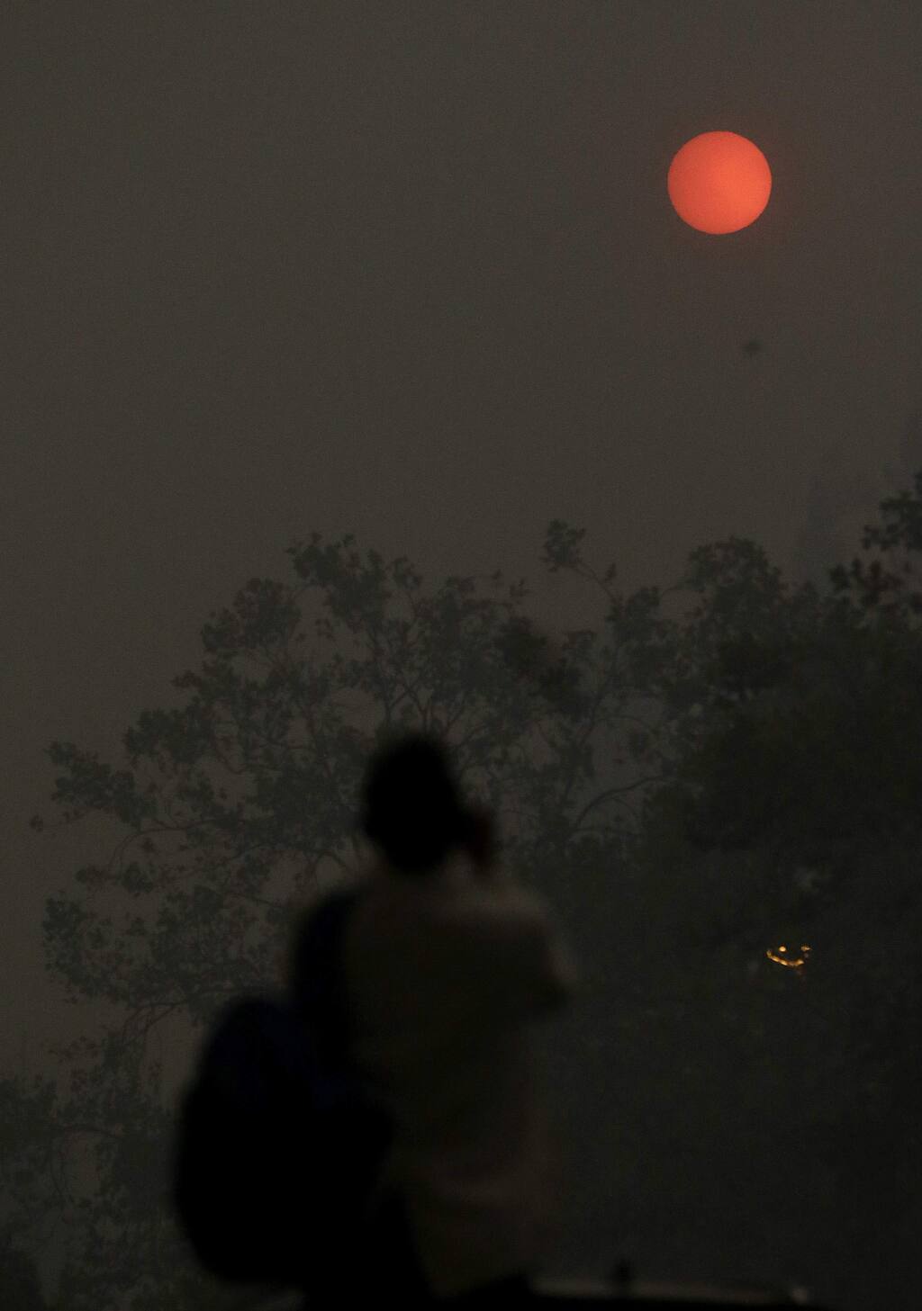 A woman takes a photo of the sun covered from smoke and haze from fires in Santa Rosa, Calif., Monday, Oct. 9, 2017. Wildfires whipped by powerful winds swept through Northern California early Monday, sending residents on a headlong flight to safety through smoke and flames as homes burned. (AP Photo/Jeff Chiu)