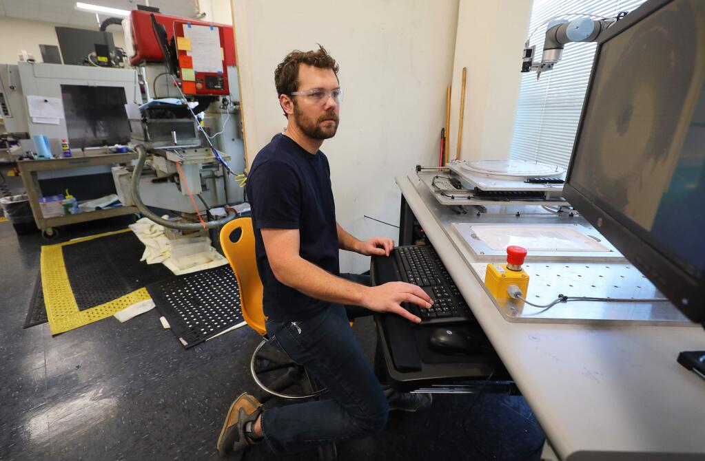 Electrical engineer Orion Leland works with a peck and place robot moving thin film optics at Alluxa, in Santa Rosa on Thursday, March 19, 2020. (Christopher Chung/ The Press Democrat)