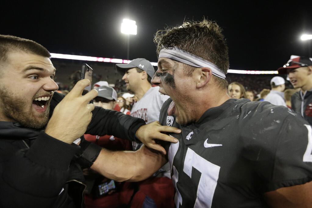 Washington State linebacker Peyton Pelluer, right, celebrates with a fan after his team won 34-20 against Oregon, in Pullman, Saturday, Oct. 20, 2018. (AP Photo/Young Kwak)