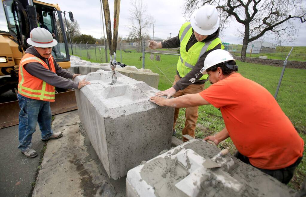 From left, Braulio Centeno, Jake Clay, and Pepe Galvez, move in to place 4,000-pound concrete blocks that will help protect the Santa Rosa's Laguna Treatment Plant on Llano Road against flooding in Santa Rosa, Monday Jan. 25. 2016. (Kent Porter / Press Democrat) 2016