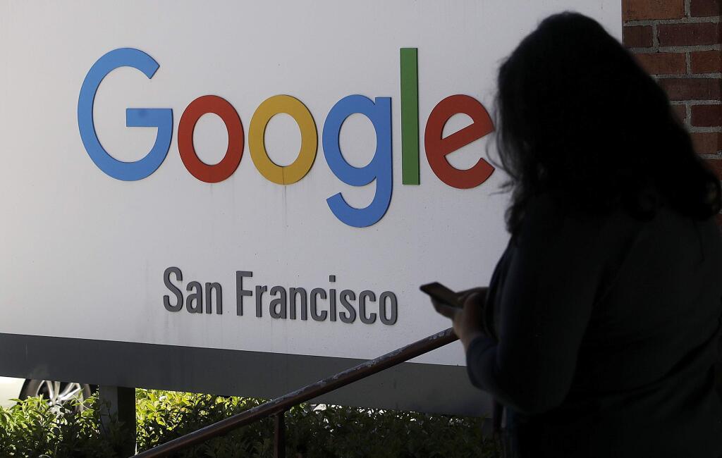 FILE - In this May 1, 2019, file photo, a woman walks past a Google sign in San Francisco. Google is making a $1 billion commitment to address the soaring price of housing in the San Francisco Bay Area, a problem that the internet company and its Silicon Valley peers helped create as the technology industry hired tens of thousands of high-paid workers. (AP Photo/Jeff Chiu, File)