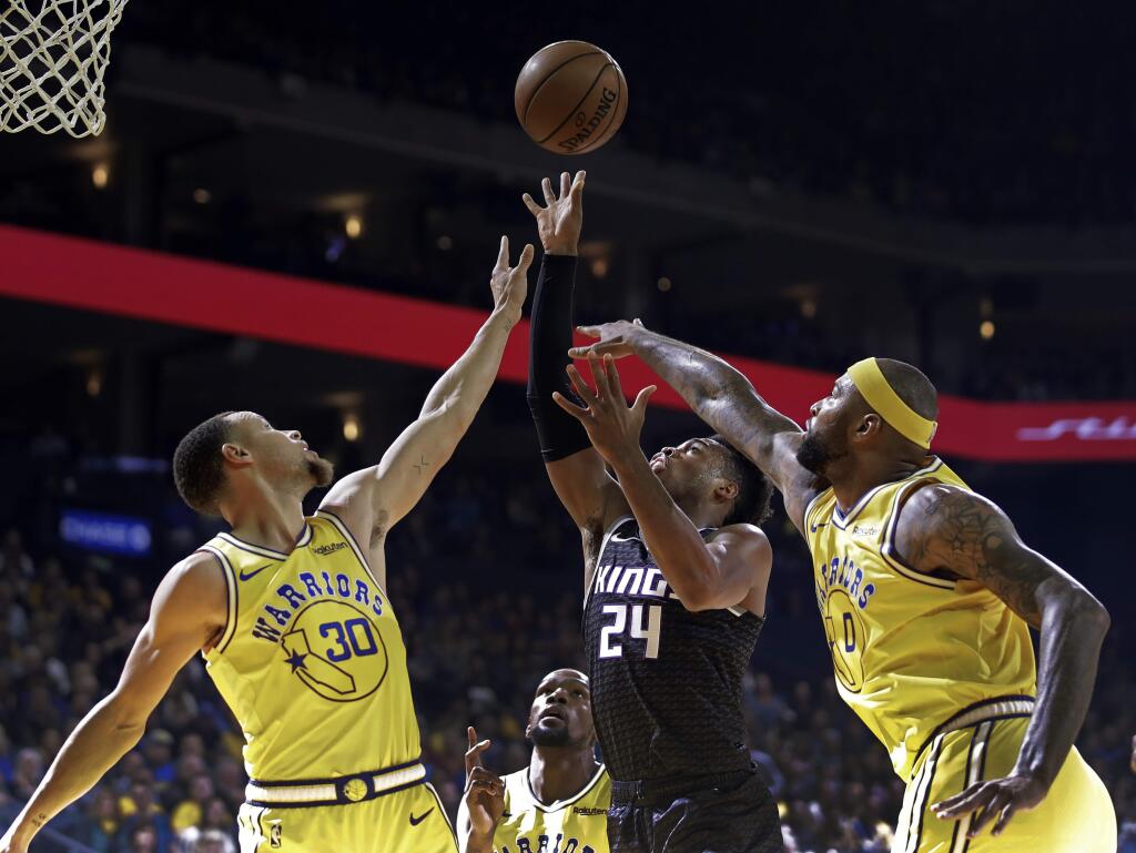 The Sacramento Kings' Buddy Hield, center, shoots between the Golden State Warriors' Stephen Curry, left, and DeMarcus Cousins during the first half Thursday, Feb. 21, 2019, in Oakland. (AP Photo/Ben Margot)