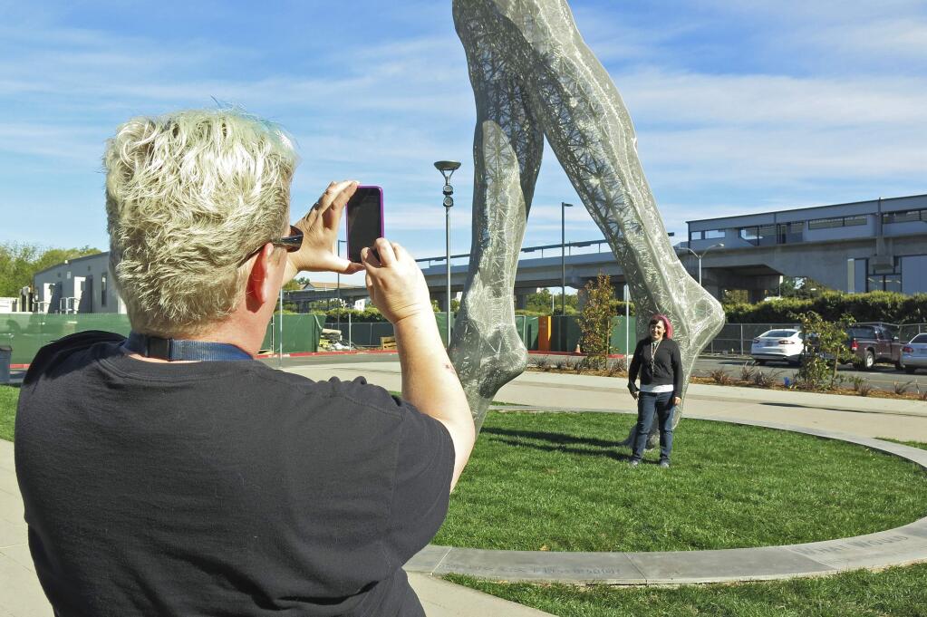 In this photo taken Wednesday Oct. 19, 2016, art teachers Jo Sutton, left, and Jennifer Jervis, right, take pictures beneath a 55-foot nude statue in San Leandro, Calif. The statue of a naked woman is stirring controversy and a lot of conversation. City officials and the sculptor of the steel nude, which was unveiled this week across from San Leandro's main commuter train stop, say they want to draw attention to 'feminine energy.' Critics say the 13,000-pound towering nude is not appropriate public art. (AP Photo/Jocelyn Gecker)