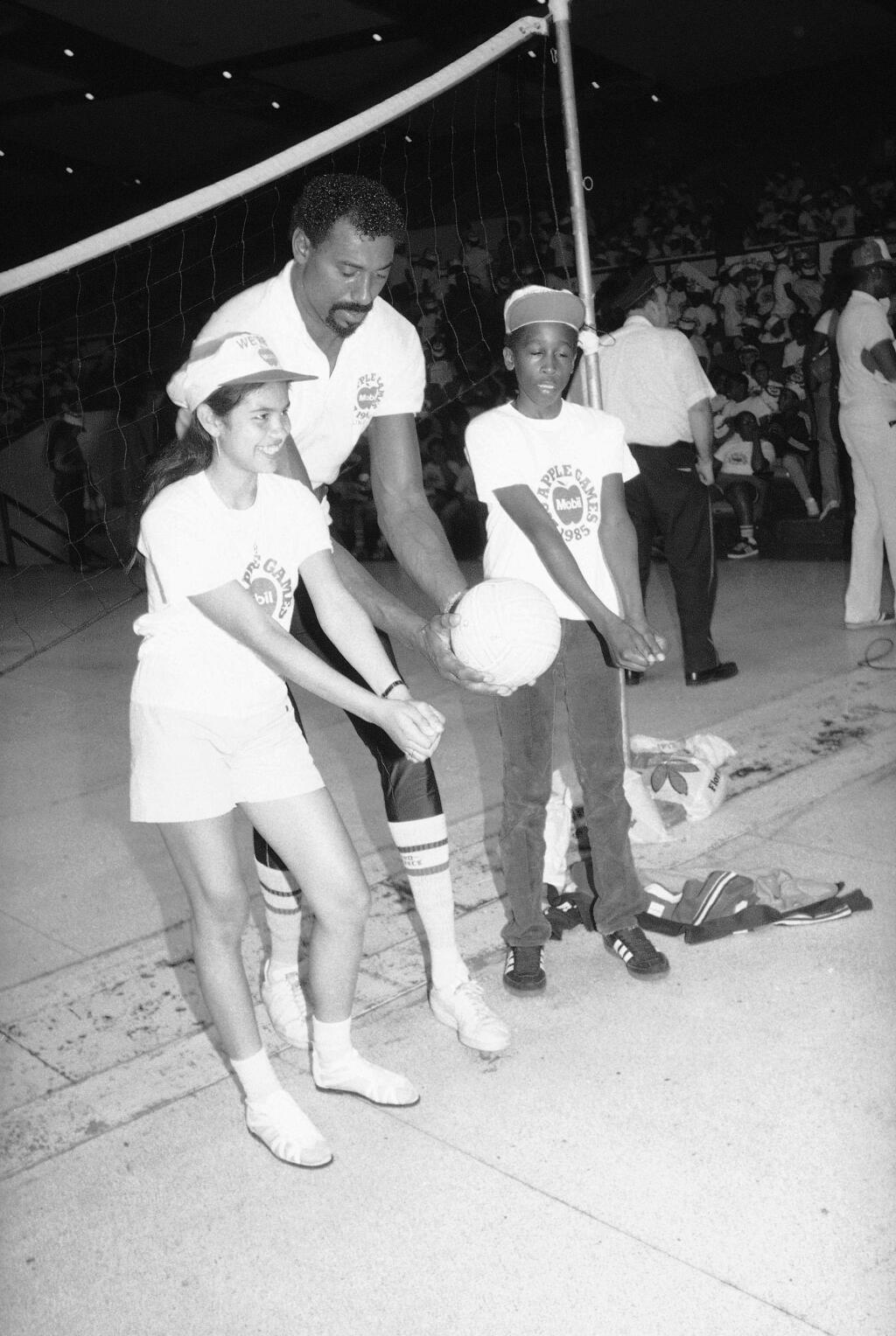 Wilt Chamberlain shows Denise Blake, left, and Lamont Wilson, both 14, the proper way to hit a volleyball in New York, Wednesday, July 17, 1985. The 7-foot-1 former basketball player offered instruction to youngster at the Mobil Big Apple Games clinic in which school-age children receive daily instruction in a wide variety of sports. (AP Photo/David Bookstaver)