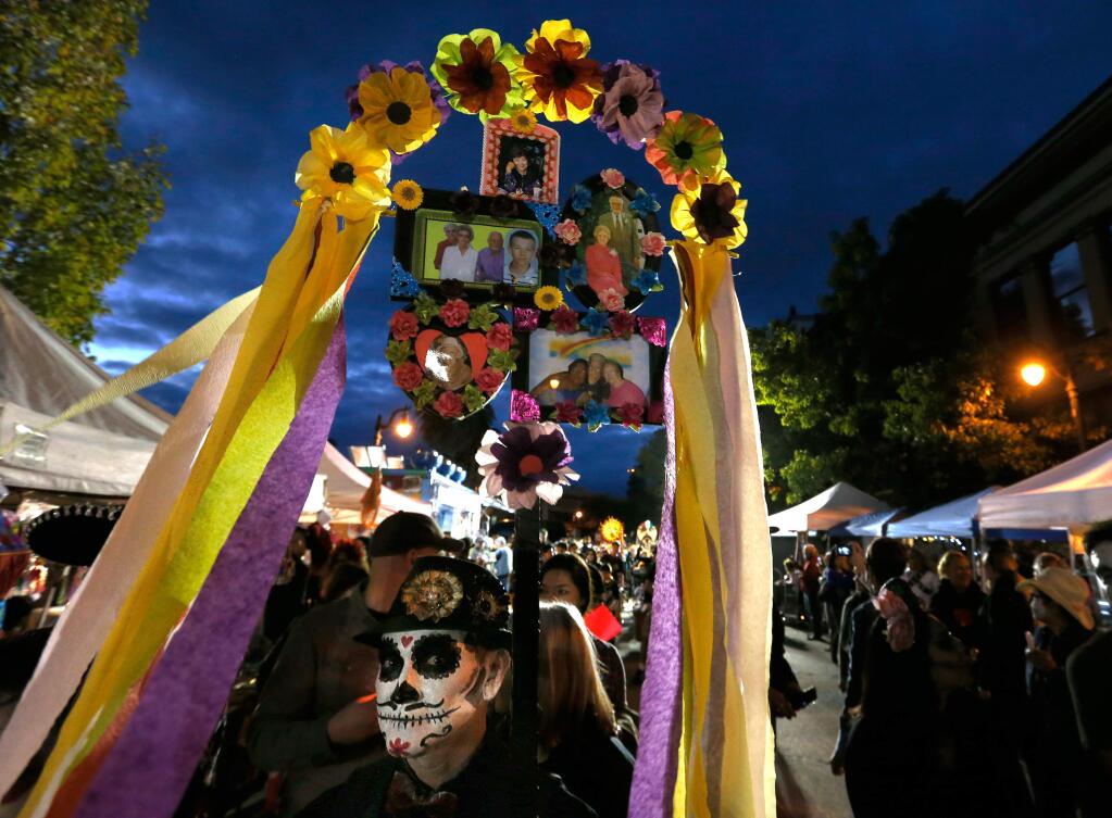 Osvaldo Espinoza carries a banner decorated with photographs of relatives and friends during the Dia de los Muertos procession in Petaluma, California on Saturday, October 29, 2016. (Alvin Jornada / The Press Democrat)