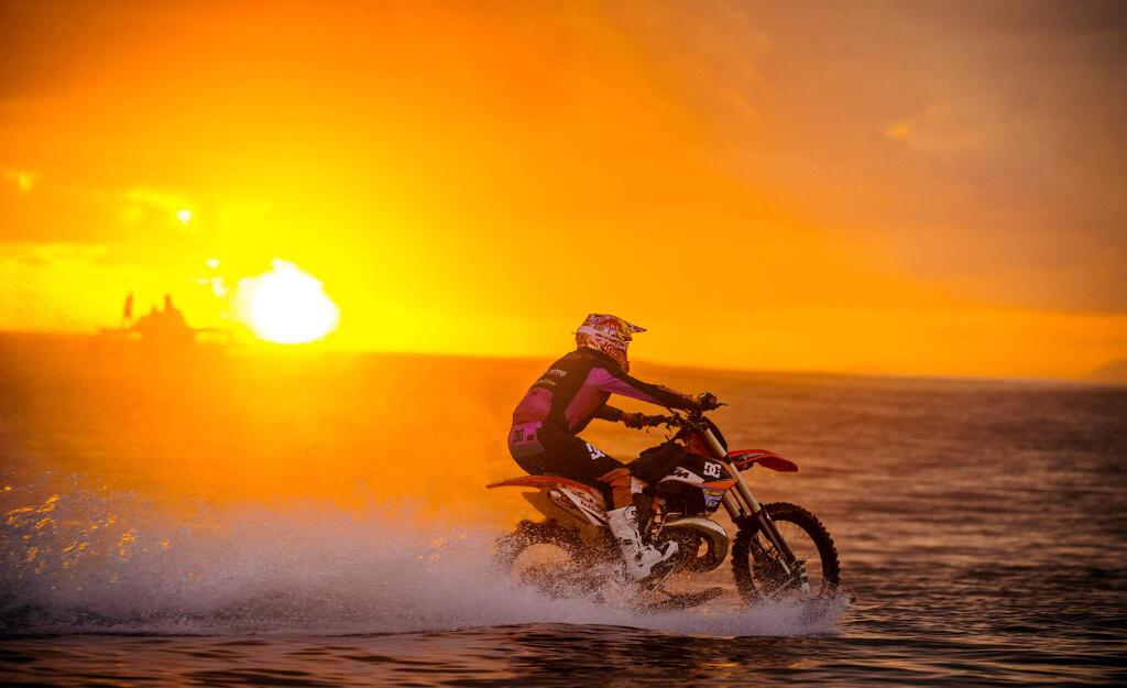 In this April, 2015, photo provided by DC Shoes, daredevil Robbie Maddison in his latest stunt rides his motorcycle across waves in Tahiti, French Polynesia, using ski-like devices on his wheels. (Mike Blabac/DC Shoes via AP)