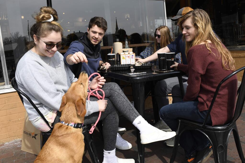 Clay Colehouse of Crownsville, Md., second from left, gives the dog Marty a treat as he and his friends, from left, Erin Carroll of Severna Park, Md., Jessica Goblin of Severna Park, Md., Travis Victorio of Millersville, Md., and Mary Fitzell of Millersville, Md., have lunch during a visit to Annapolis, Monday, March 16, 2020. Maryland Gov. Larry Hogan ordered the closure of bars, restaurants, gyms and movie theaters across the state in response to coronavirus beginning at 5 p.m. Monday. Drive-thru, carryout and delivery service will still be allowed. The friends gathered for lunch because they are home from college. (AP Photo/Susan Walsh)