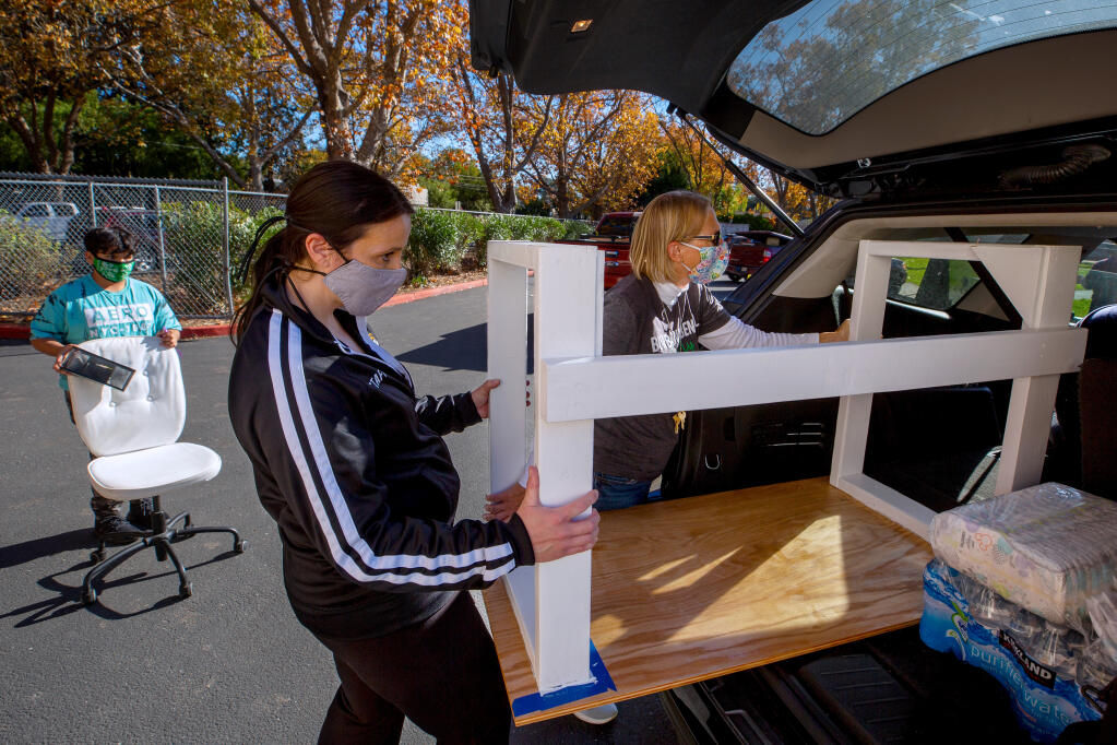 Luther Burbank Elementary School principal Debi Cardozo and sixth grade teacher Debbie Crapeau, right, help load a handmade desk into a vehicle for student Rudy Magaña, 11, at far left, in Santa Rosa, California, on Friday, November 20, 2020. Cardozo led committee discussion over potentially changing the name of the school. (Alvin A.H. Jornada / The Press Democrat)