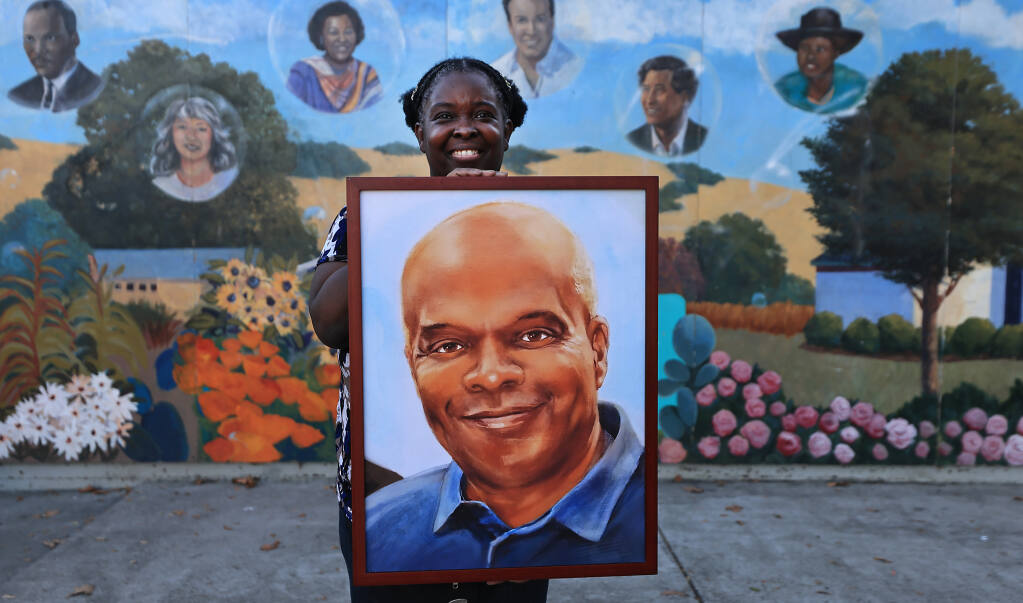 Evette Minor, an organizer of South Park Day and Night Festival, with a portrait of Vince Harper, a longtime employee of Community Action Partnership of Sonoma County who died last November, was also added to the mural in the background by Art Start, Saturday, Sept. 24, 2022 in Santa Rosa. (Kent Porter / The Press Democrat) 2022