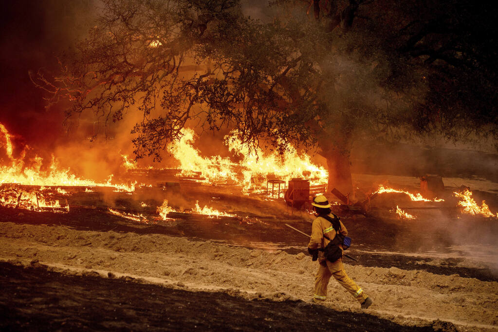 FILE - In this Oct. 1, 2020 file photo a firefighter passes flames while battling the Glass fire in a Calistoga, Calif., vineyard.  (AP Photo/Noah Berger, File)
