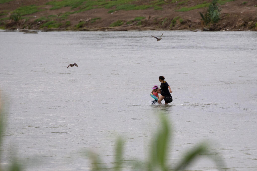 A woman and a child cross the Rio Grande river towards the U.S. in Eagle Pass, Texas, Sunday May 22, 2022. Little has changed in what has quickly become one of the busiest corridors for illegal border crossings since a federal judge blocked pandemic-related limits on seeking asylum from ending Monday. (AP Photo/Dario Lopez-Mills)