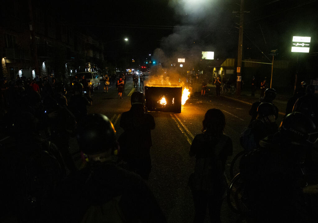 A waste receptacle is set on fire near the Portland Police Association building during a protest in Portland, Ore., on Tuesday, Aug. 4, 2020.  A riot was declared early Wednesday during demonstrations in Portland after authorities said people set fires and barricaded public roadways.(Dave Killen /The Oregonian via AP)