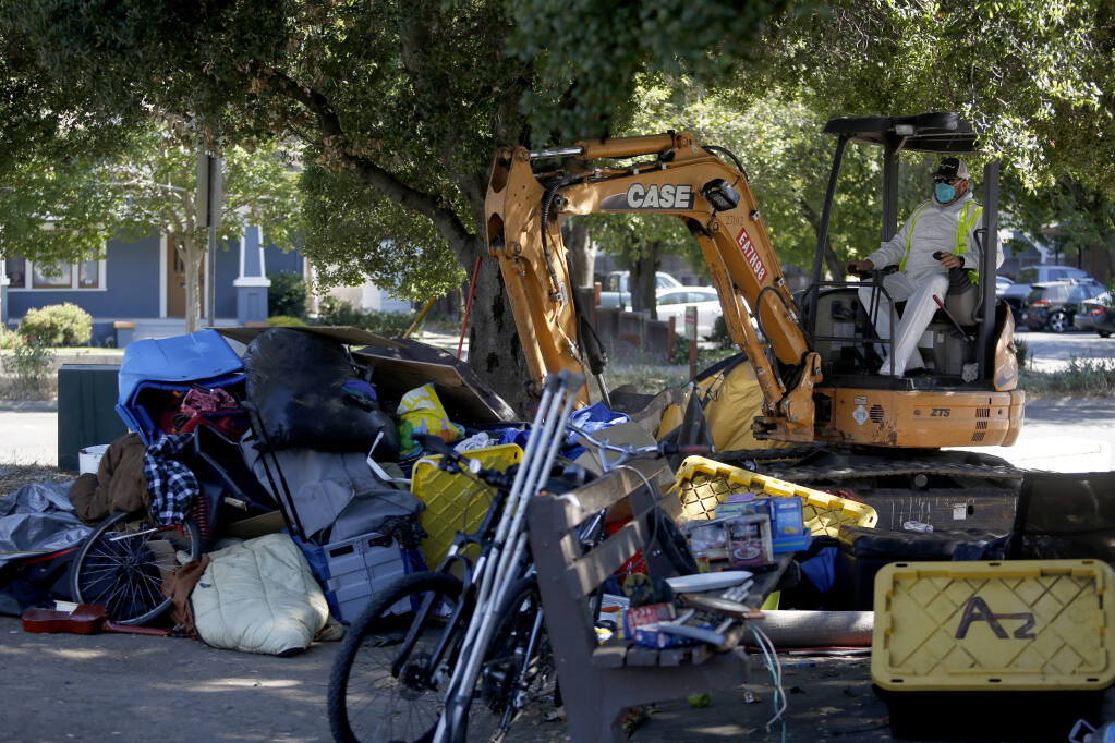 Santa Rosa public works employee Deric Glen uses a excavator to dispose of personal belongings left behind at a homeless encampment at the corner of Fourth Street and College Avenue in Santa Rosa on Tuesday, June 29, 2021. (Beth Schlanker/The Press Democrat)