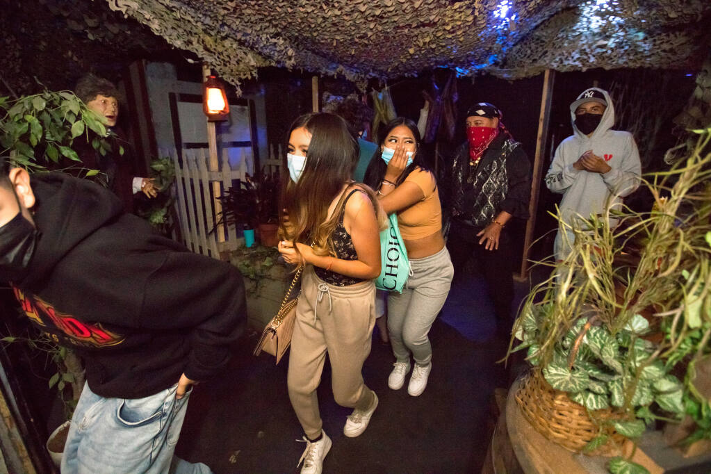 From left, Michael Crews, 15, Kelly Crews, 14, and Liz Lopez, 14, and Leo Alvez, 15, (back right), all from Santa Rosa, run as a character in a red bandanna follows them, at the Blind Scream Witch House, in Santa Rosa, on Sunday, Oct. 10, 2021. (Photo by Darryl Bush / For The Press Democrat)