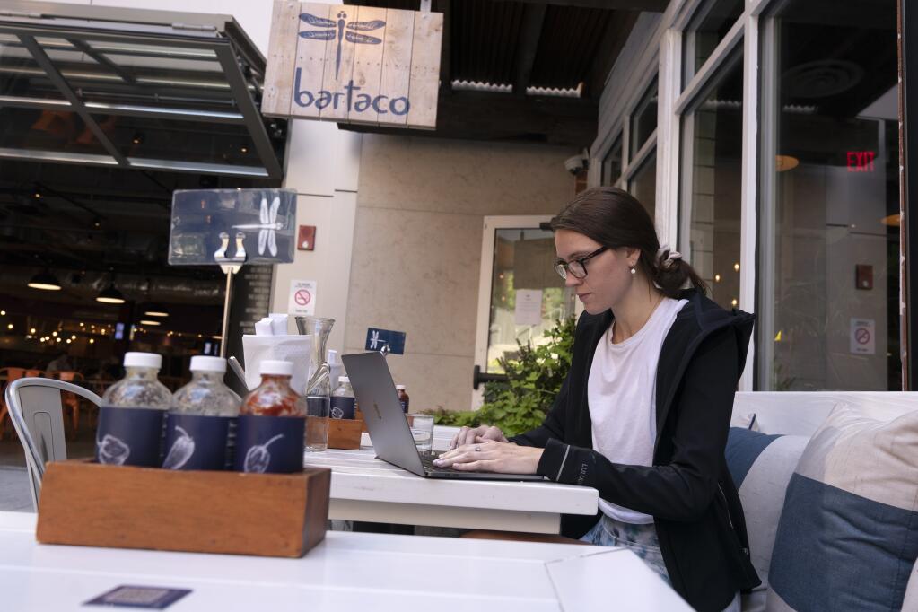 Baylee Bowers works on her computer after ordering and paying for her meal using her cell phone at Bartaco in Arlington, Va., on Thursday, Sept. 2, 2021. The restaurant uses an automated app for ordering and payments. Instead of servers they use "food runners" to get orders to tables. (AP Photo/Jacquelyn Martin)