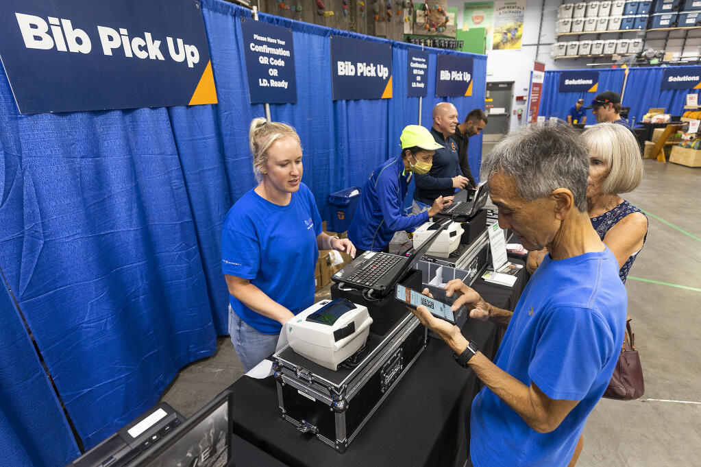 Steven and Denise Watanabe, of Santa Clarita, right, pick up their racing bibs for the Santa Rosa marathon from Leah Horvath at Sports Basement  August 26, 2022.    (John Burgess/The Press Democrat)