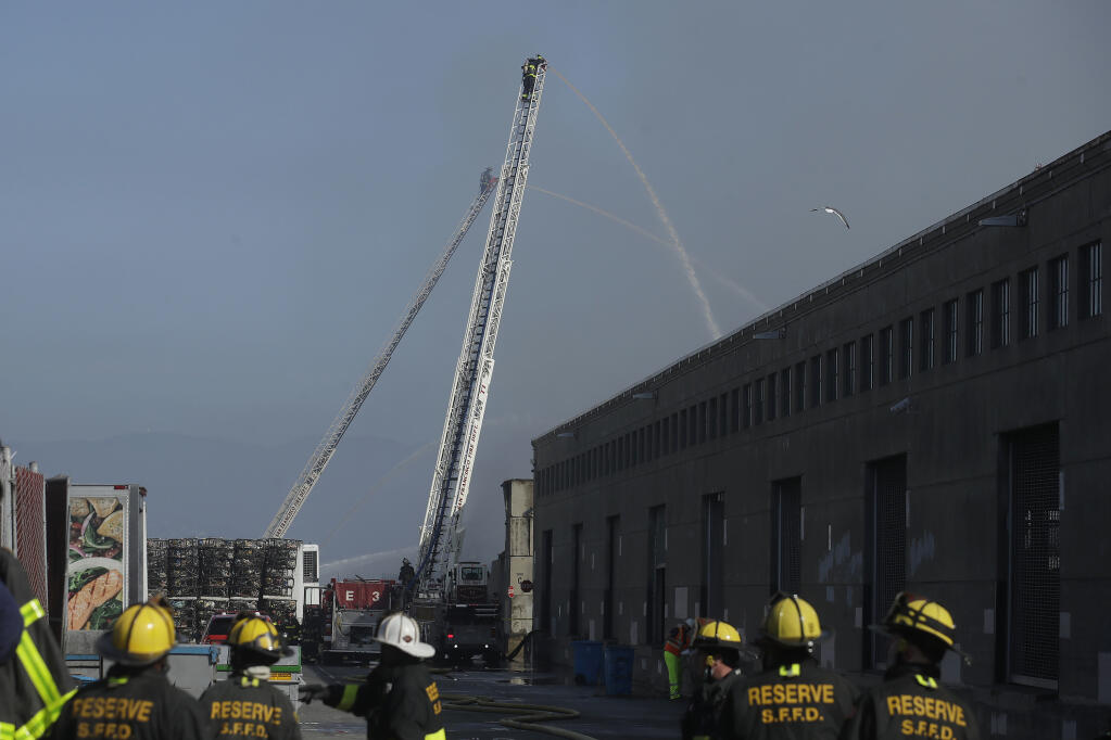 FILE - In this May 23, 2020, file photo, a firefighter sprays into a warehouse after a fire broke out before dawn at Fisherman's Wharf in San Francisco. Commercial fishers are suing the Port of San Francisco, claiming gross negligence that resulted in a massive fire in May that destroyed a warehouse the size of a football field where the fishers stored their gear. The fishers claim in a lawsuit filed Wednesday, Dec. 16, 2020, that the port knew homeless people entered the warehouse and cooked in it, failed to maintain its aging electrical system, stored flammable materials in the building and even failed to ensure enough water on the premises to fight the fire. (AP Photo/Jeff Chiu, File)