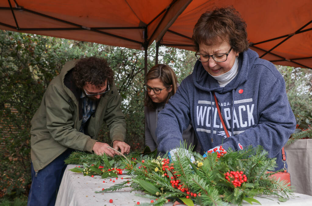 Rosemary Lely, right, makes a wreath, while Nicholas Shepard, left, helps Renise Chiotti tie off her wreath during Art Escape’s Holiday Craft Fest in Sonoma, Sunday, Dec. 11, 2022.  (Christopher Chung/The Press Democrat)