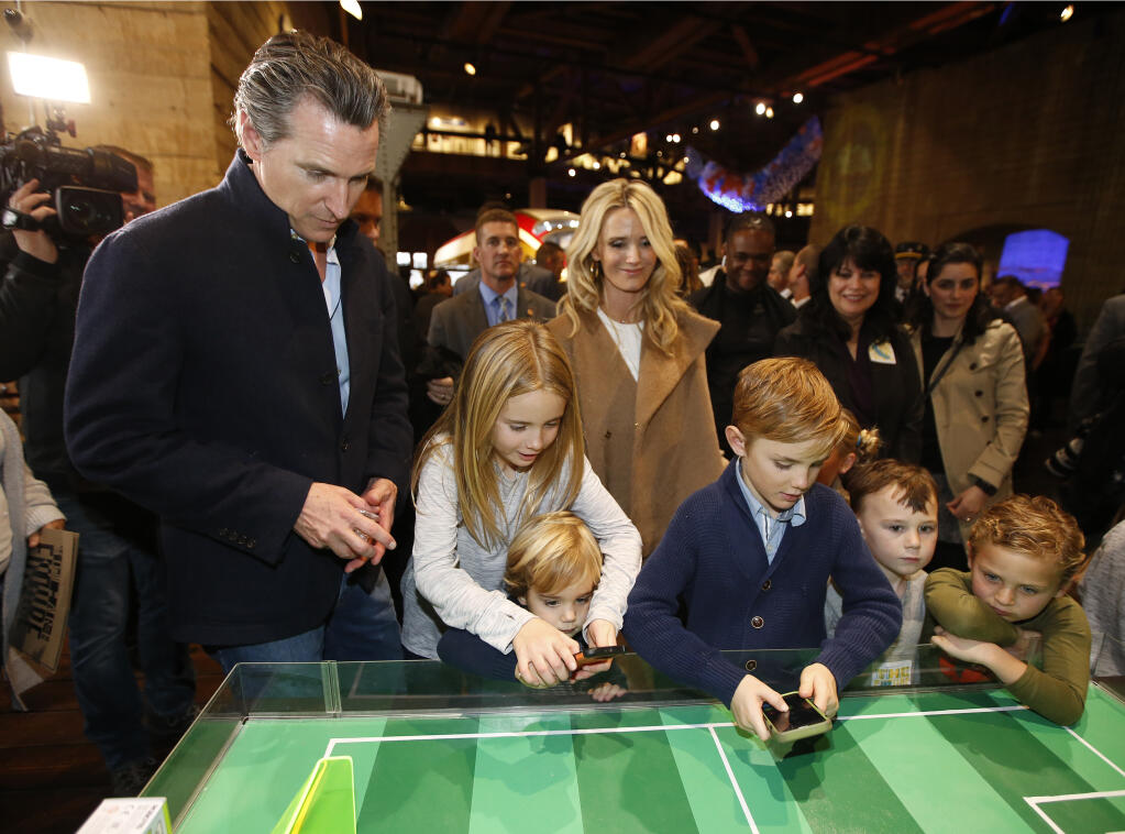 FILE - In this Jan. 6, 2019, file photo Governor-elect, Lt. Gov. Gavin Newsom, left, and his wife, Jennifer Siebel Newsom, center, watch their children, daughter Montana, second from left, and sons, Dutch, foreground, and Hunter, foreground fourth from left, operate robot games at the California Railroad Museum, Sacramento, Calif. Newsom said Friday, Oct. 30, 2020, his children are among those resuming in-person classes after months of distance learning due to the coronavirus pandemic. (AP Photo/Rich Pedroncelli, File)