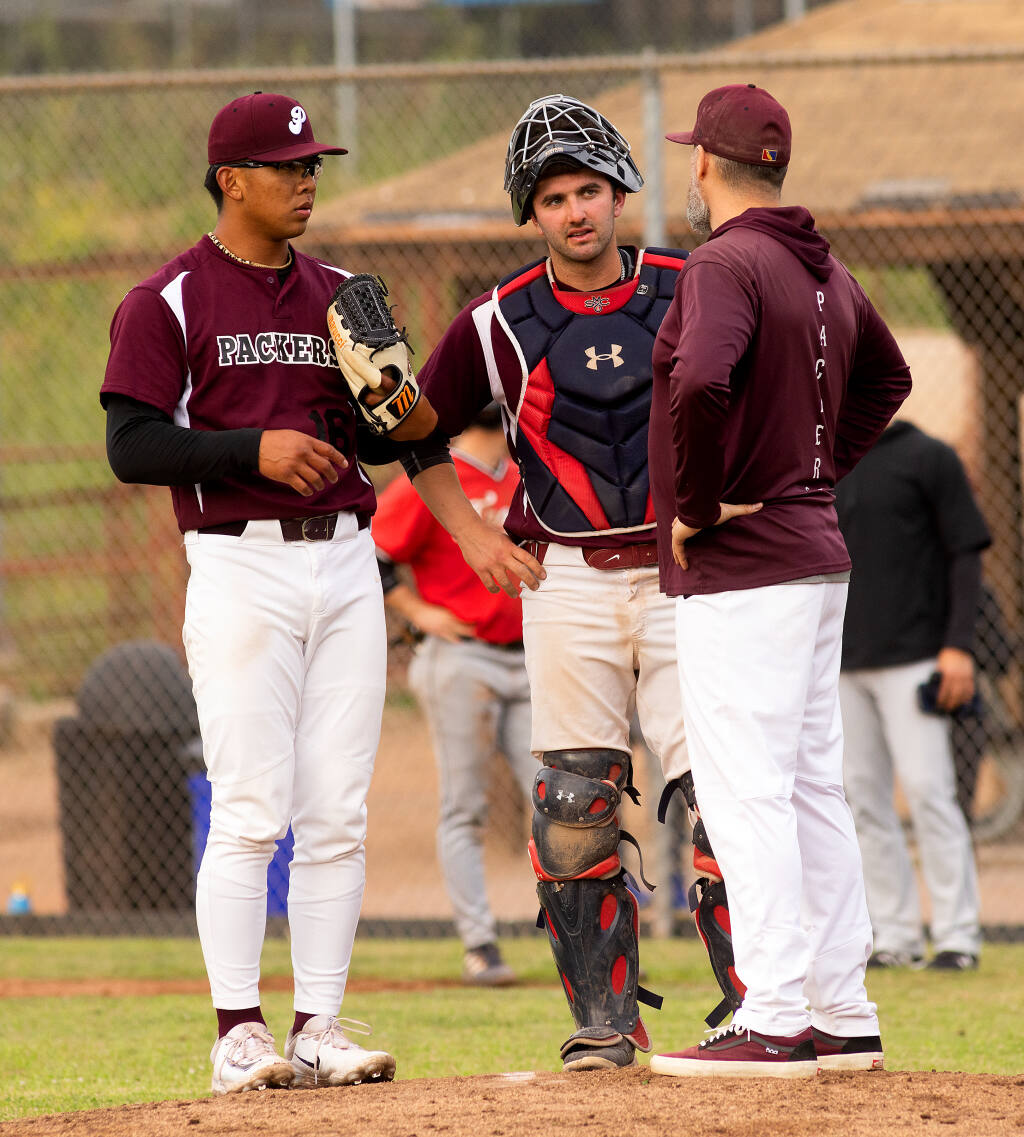Healdsburg Prune Packers coach Joey Gomes, right, meets at the mound with catcher Blake MacDonald and pitcher Marv Guarin during last month’s season opener.  (John Burgess / The Press Democrat)