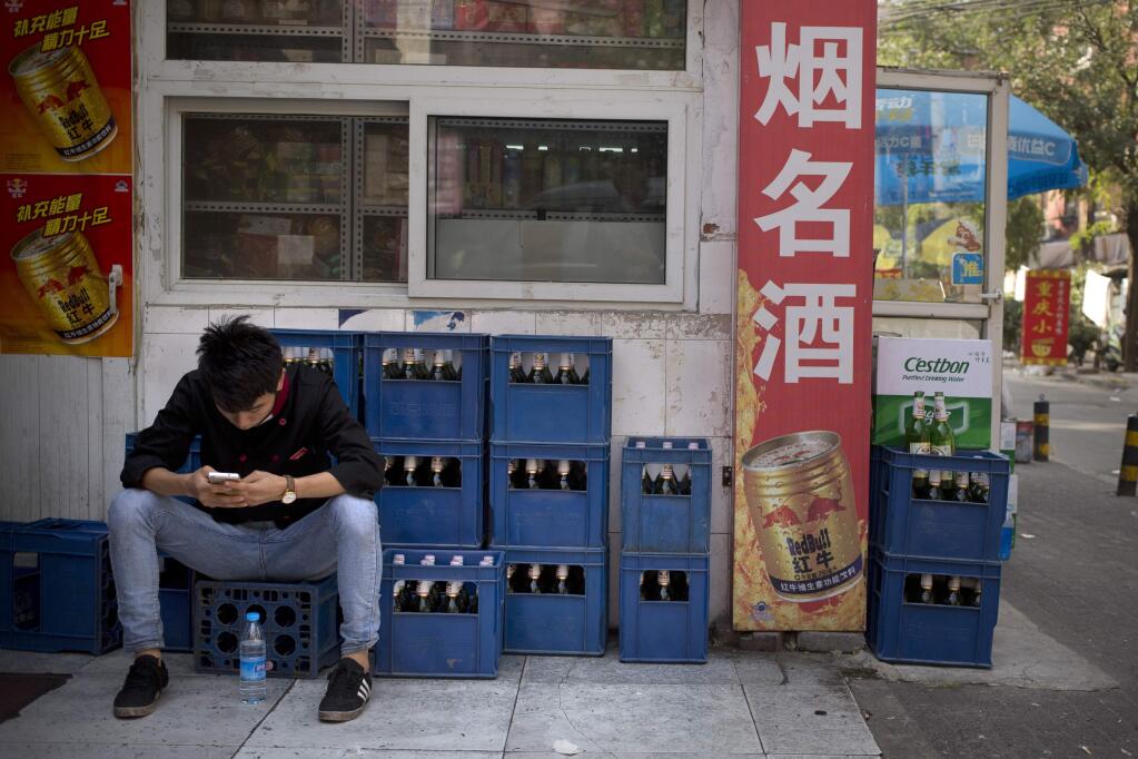 FILE - In this Thursday, Oct. 15, 2015, photo, a restaurant worker sits on crates of beer outside a convenience store as he uses his smartphone in Beijing. Hundreds of craft beer enthusiasts, investors and brewers are attending an exhibition in Shanghai dedicated to expanding the palette of Chinese consumers and promoting sales of high-end brews. (AP Photo/Mark Schiefelbein, File)
