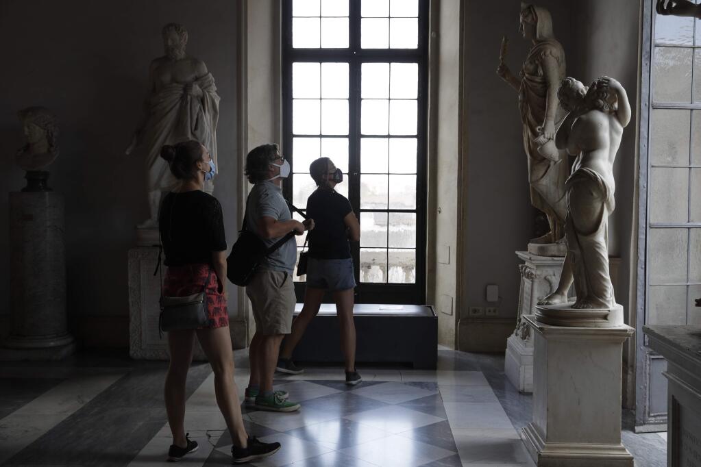Visitors wearing a face masks to prevent the spread of COVID-19 admire statues in the Rome Capitoline Museums, including the second century A.D. Roman marble statue 'Cupid and Psyche', at right, Tuesday, May 19, 2020. In Italy, museums were allowed to reopen this week for the first time since early March, but few were able to receive visitors immediately as management continued working to implement social distancing and hygiene measures, as well as reservation systems to stagger visits to museums in the onetime epicenter of the European pandemic. (AP Photo/Alessandra Tarantino)