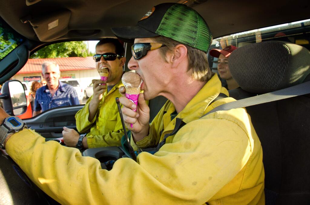 In this photo shot Friday, July 24, 2015, fire fighters form Liberty Wildfire Inc., out of Twisp, Wash., stop for ice cream on thier way up to the Blue Creek Fire near Walla Walla, Wash. Charles Stanger, background, organized volunteers to hand out ice cream cones and popcicles along the road to the fire. (Greg Lehman/Walla Walla Union-Bulletin via AP)