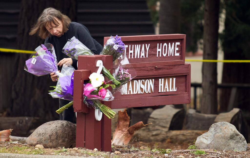 An employee with Veterans Home of California in Yountville, who did not want to give her name, places flowers on the sign for the Pathway Home, where former client Albert Wong, 36, killed three mental health workers and himself on Friday. (photo by John Burgess/The Press Democrat)
