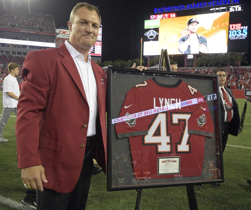 Former Tampa Bay Buccaneers safety John Lynch, center, poses with his jersey during a ceremony inducting him in the team's Ring of Honor during an NFL football game between the Tampa Bay Buccaneers and the Atlanta Falcons in Tampa, Fla., Thursday, Nov. 3, 2016. (AP Photo/Phelan M. Ebenhack)
