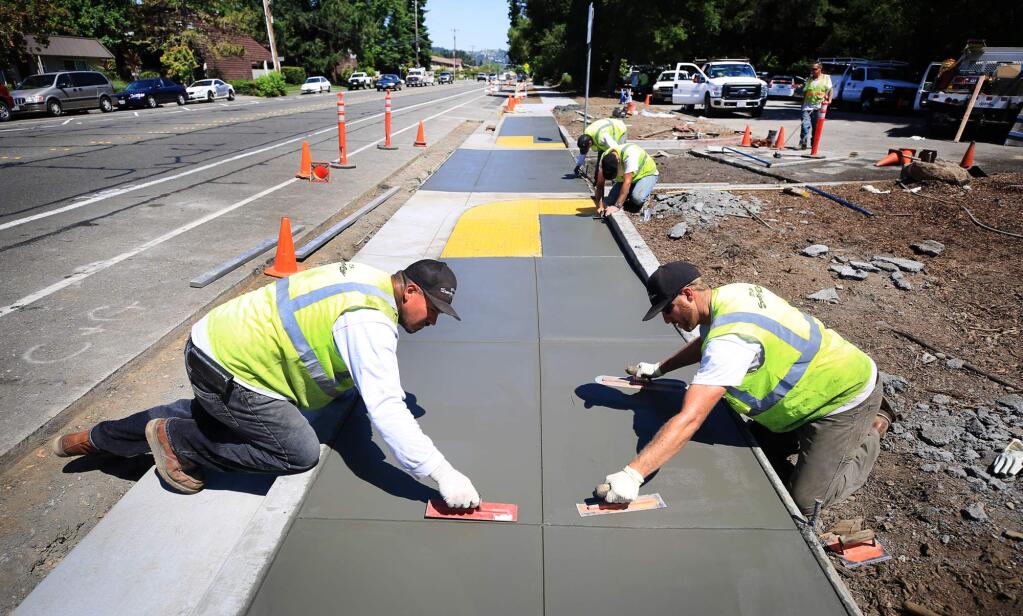 Santa Rosa city workers, Ramon Contreras, left, Josh Carstensen put the finishing touches on ADA accessible sidewalks fronting Howarth Park on Summerfield road in Santa Rosa, Tuesday June 20, 2017. (Kent Porter / Press Democrat) 2017